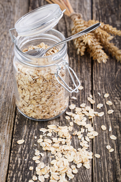 Oat flakes spilled out from jar and wheat. - Photo, Image