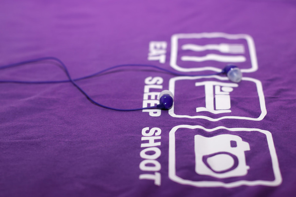 Вакуумні сині навушники лежать на фіолетовій футболці
 - Фото, зображення