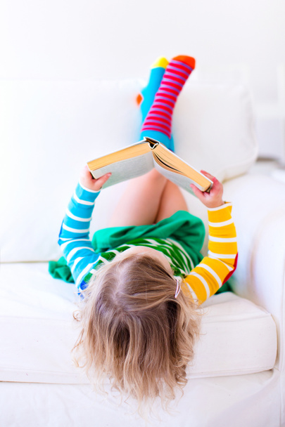 Kleines Mädchen liest ein Buch auf einer weißen Couch - Foto, Bild