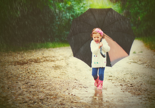 happy baby girl with an umbrella in the rain runs through - Fotografie, Obrázek
