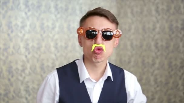 Zabawny facet z kapeluszem, okulary i fałszywe wąsy stwarzające na jasnym tle - Materiał filmowy, wideo
