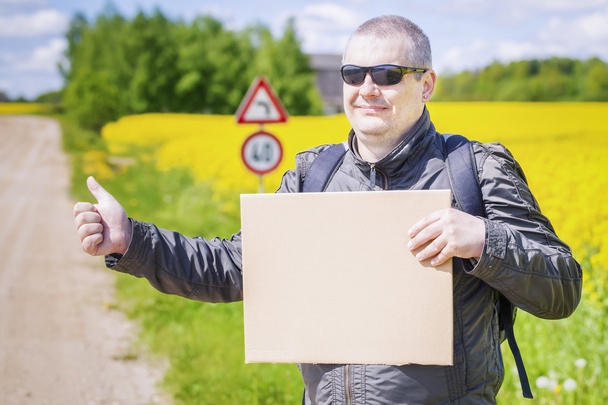 Hiker with cardboard try to stop car on rural road - Photo, Image