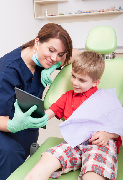 Niño feliz paciente en el dentista utilizando la tableta inalámbrica
 - Foto, imagen