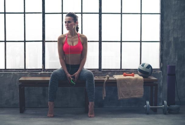 Fit woman sitting on bench in workout gear listening to music - Photo, image