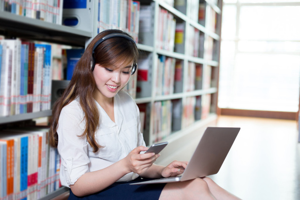 студентка с помощью ноутбука и мобильного телефона в библиотеке
 - Фото, изображение