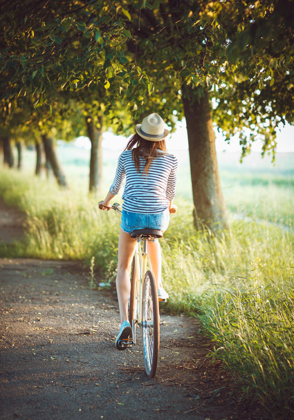 Lovely young woman in a hat riding a bicycle outdoors. Active pe - 写真・画像
