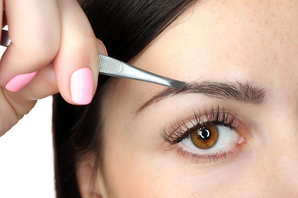 Young woman plucking eyebrows with tweezers close up - Fotó, kép