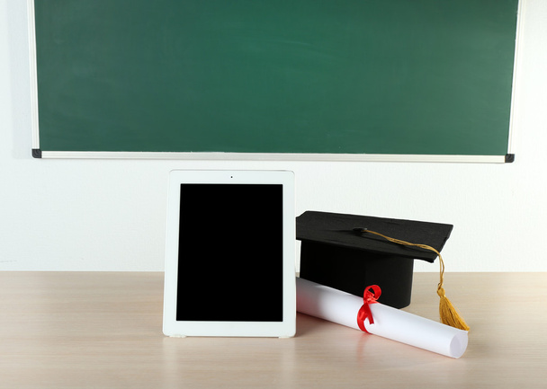 Graduation cap with tablet and diploma on table in class - Valokuva, kuva