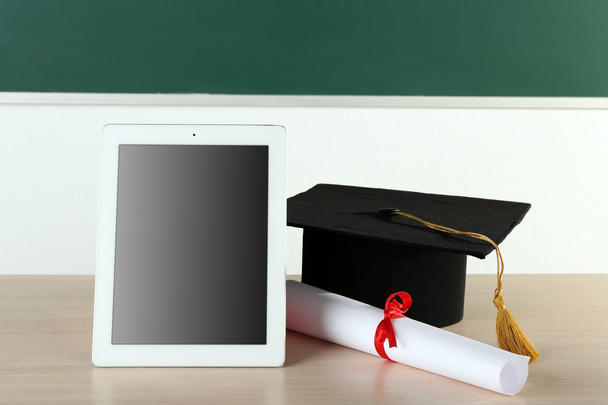 Graduation cap with tablet and diploma on table in class - Fotoğraf, Görsel