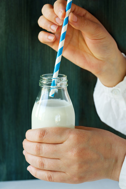 bottle of milk with striped straw in the hands of - Fotoğraf, Görsel