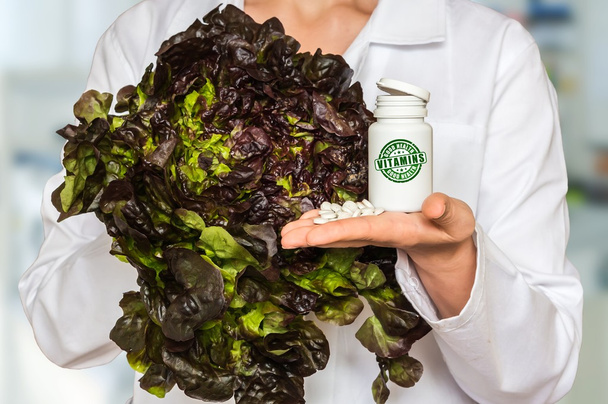 Young doctor holding lettuce and bottle of pills with vitamins and compare them - Foto, afbeelding