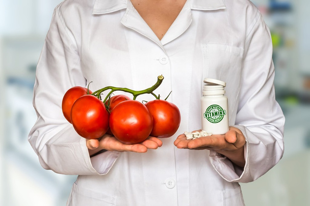 Jovem médico segurando tomates e garrafa de comprimidos com vitaminas e compará-los
 - Foto, Imagem