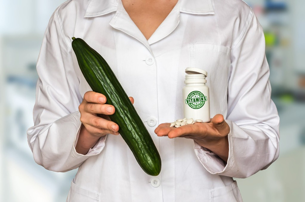 Jeune médecin tenant concombre frais et bouteille de pilules vitamines et les comparer
 - Photo, image
