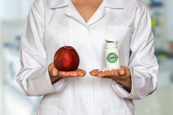 Молодой врач держит яблоко и бутылку таблеток с витаминами и сравнить их
 - Фото, изображение
