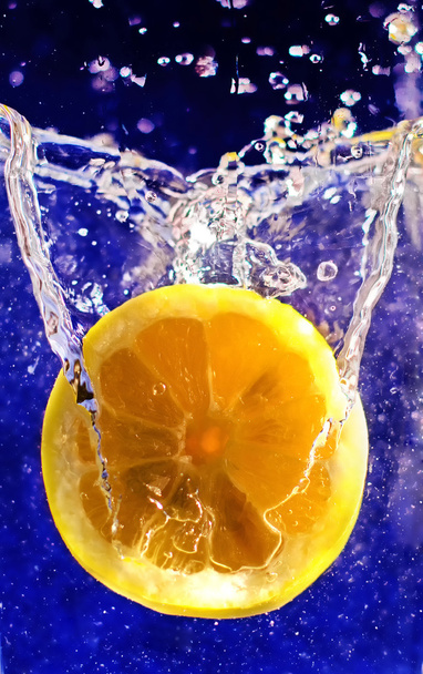 Свіжа половина лимона в бризках води на темно-синьому фоні
 - Фото, зображення