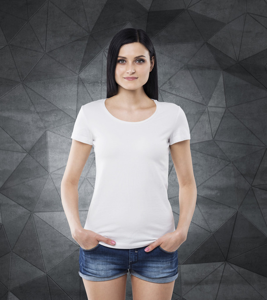 Brunette girl in a white t-shirt and denim shorts. Contemporary dark grey background. - Zdjęcie, obraz