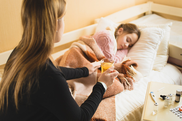 caring mother giving hot tea to daughter lying in bed - Foto, Imagen