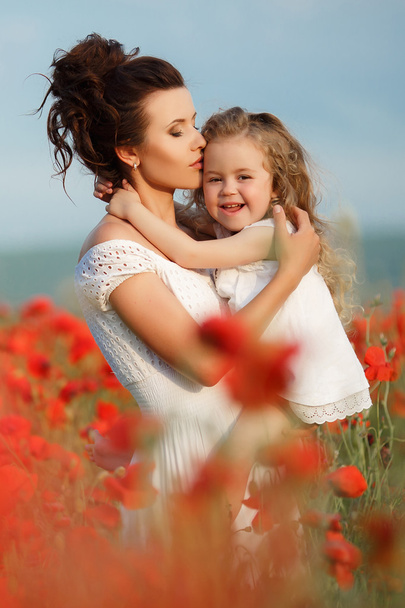 Mother with her little daughter in her arms in a field of blooming poppies. - Foto, Imagen