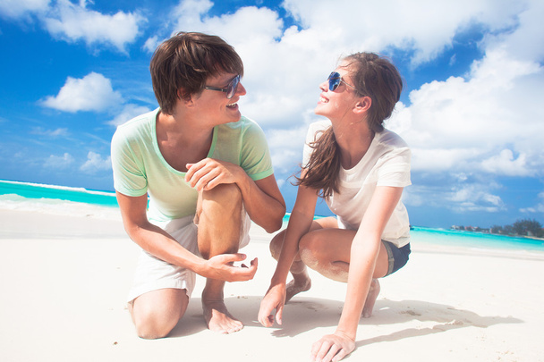 Fechar-se de feliz jovem casal caucasiano em óculos de sol sorrindo na praia e olhando para o sol
 - Foto, Imagem
