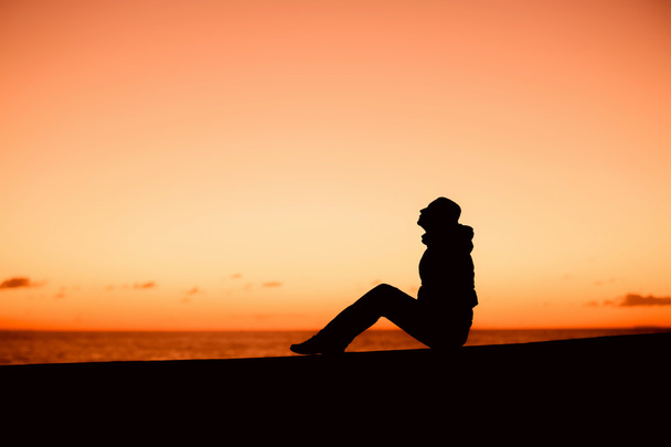 Silhouette d'une femme assise sur le bord sur un beau coucher de soleil rouge
 - Photo, image