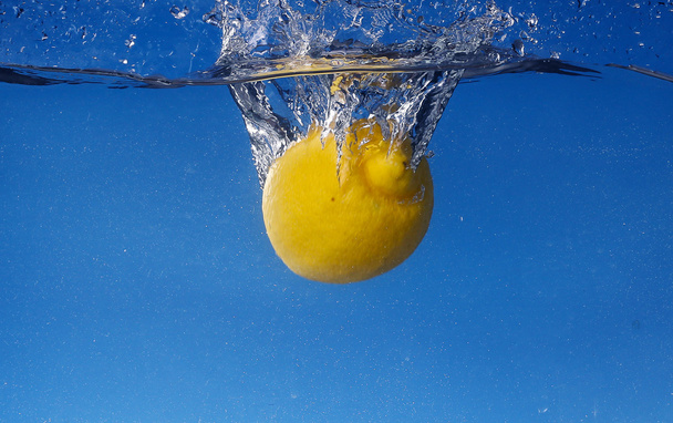 Whole lemon dropped in water against gradient blue background - Foto, Imagem