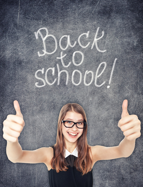 Happy schoolgirl showing thumbs up on the chalkboard background - Foto, afbeelding