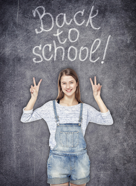 Happy schoolgirl showing victory sign on the chalkboard backgrou - Fotoğraf, Görsel