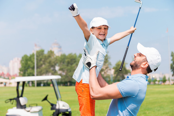 man picking up his son on golf course - Zdjęcie, obraz