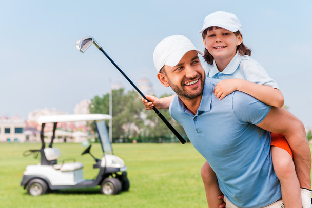 man piggybacking son on golf course - Foto, immagini