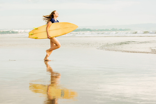 Красива сексуальна дівчина-серфер на пляжі під час заходу сонця впадає в океан, жовта дошка для серфінгу в її руках. Здорове життя, спортивна концепція з копійкою
 - Фото, зображення