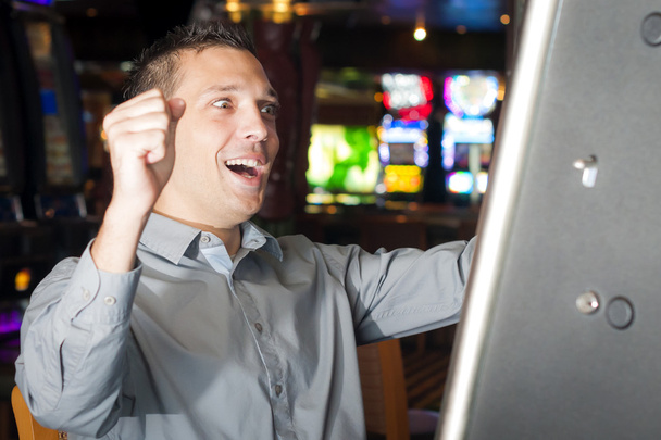 A 20-as, hajzselé, és egy szürke pólót viselő fiatal férfi játszik egy slot machine - Fotó, kép