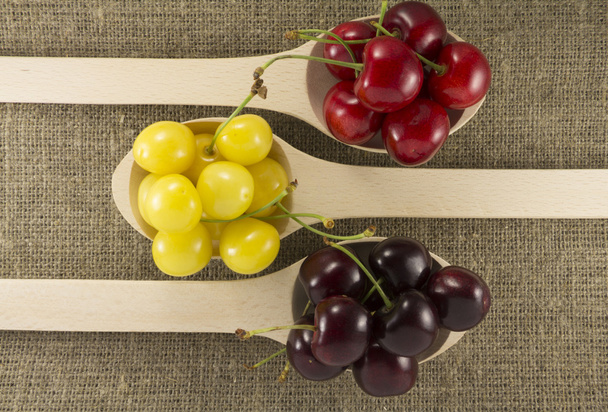 Colorful cherries in a wooden spoon on a natural fabric - Photo, Image