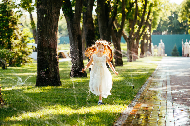 happy little girl running through the spray of water in the park - Fotoğraf, Görsel