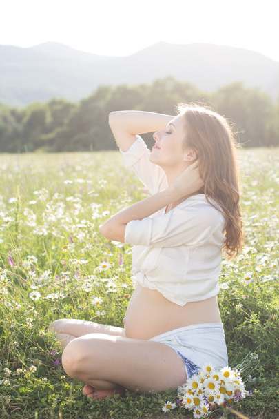 Pregnant smiling woman on field in sunset lights - Foto, immagini