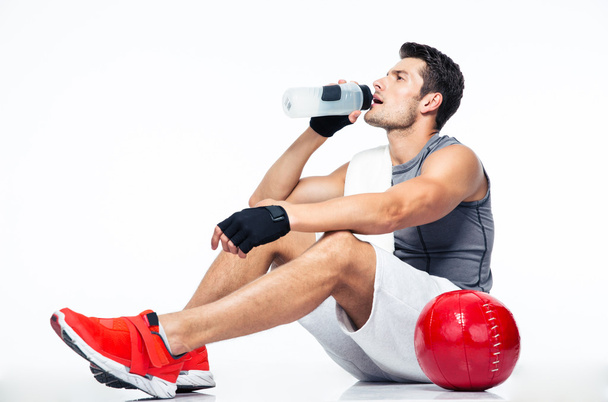 Fitness man sitting on the floor and drinking water - Fotó, kép