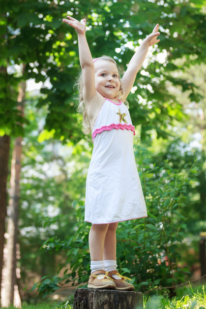 Blond dziewczynka stałego z podniesione ręce na drzewo giczoł pełnej długości - Zdjęcie, obraz