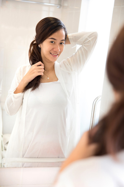 鏡で笑顔ながら彼女の髪を結ぶ美しいアジアの女性 - 写真・画像