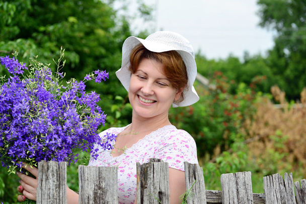 Woman with   wildflowers near  wooden fence in the village - Foto, Imagen