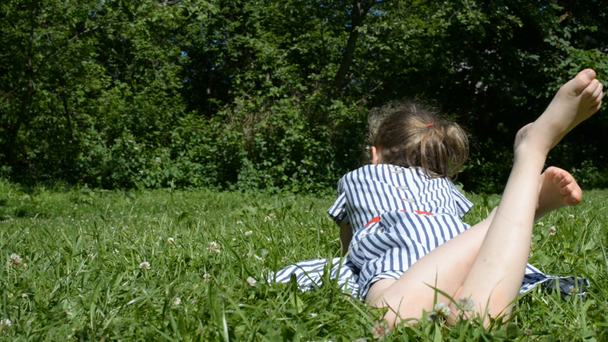 Klein meisje liggend op groen gras in het Park. - Video