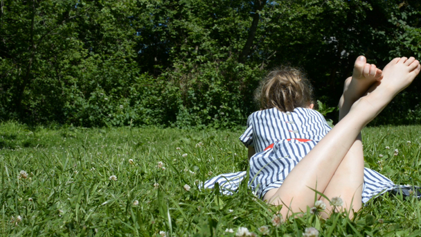Parkta yeşil çimenlerin üzerinde yatan küçük kız. - Video, Çekim