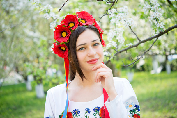 hymyilevä tyttö kansallisissa vaatteissa kukkivassa puutarhassa
 - Valokuva, kuva