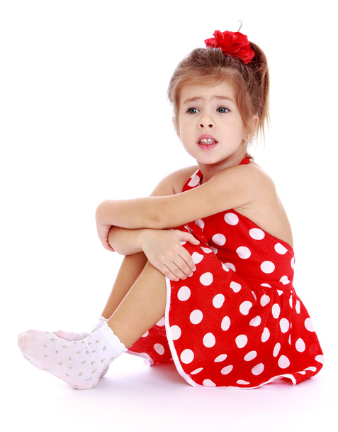 Pretty little girl in a red polka-dot dress and white socks is s - Foto, afbeelding