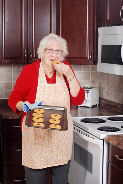 Senior woman eating fresh cookie - Valokuva, kuva