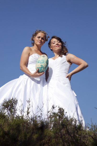dos novias con pelota de rugby contra fondo azul cielo
 - Foto, imagen