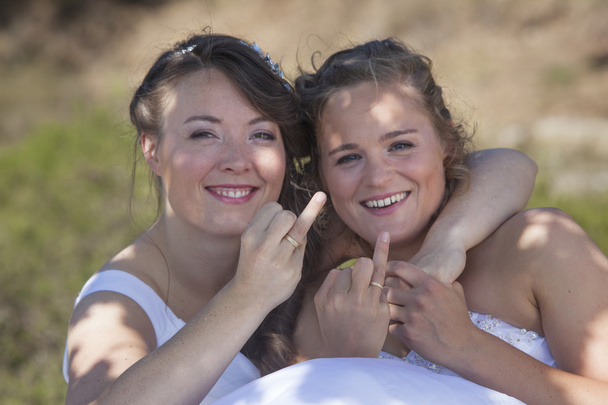 two brides smile and show their wedding rings in nature surround - Photo, Image