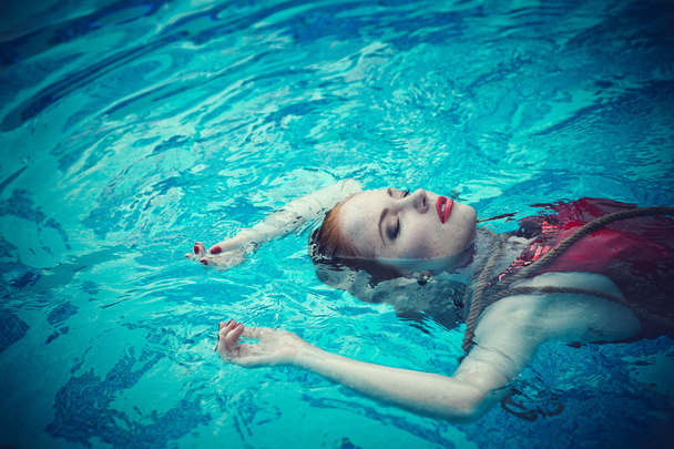 νέα σέξι γυναίκα που επιπλέει στην πισίνα με κόκκινο φόρεμα. ομορφιά πυροβόλησε - Φωτογραφία, εικόνα