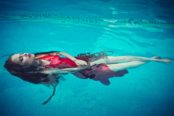 Jovem mulher sexy flutuando na piscina em vestido vermelho. tiro de beleza
 - Foto, Imagem