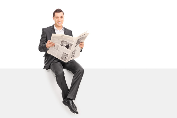 Businessman holding a newspaper seated on a panel  - Фото, зображення