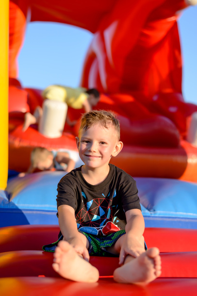 Lächelnder kleiner Junge sitzt auf einer Hüpfburg - Foto, Bild