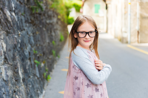 Outdoor portrait of a cute little girl in a city, wearing eyeglasses and dress - Photo, Image
